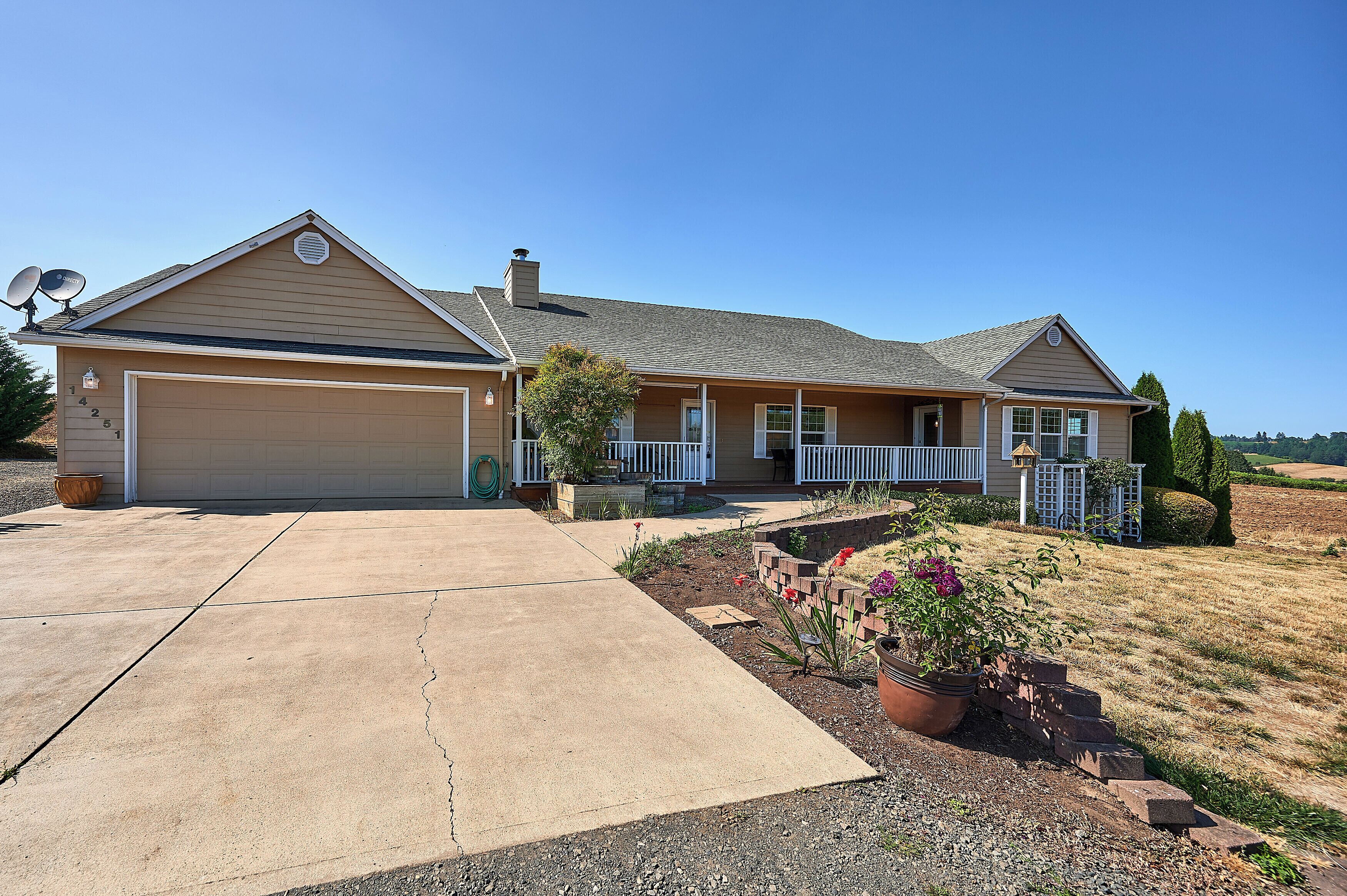 A two-story house with a garage, a covered porch, and a landscaped front yard with potted plants and a brick pathway.