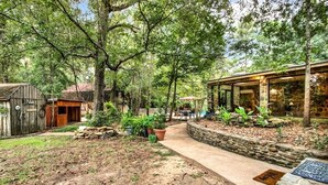 A rustic cabin with a stone pathway leading to a glass-enclosed dining area, surrounded by lush greenery. - 8 acres of fun & relaxation in a beautiful Rock Cottage with a pool and hot tub (Tomball)