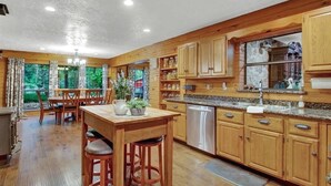 A spacious kitchen with wooden cabinets, a granite countertop, and a dishwasher. - 8 acres of fun & relaxation in a beautiful Rock Cottage with a pool and hot tub (Tomball)
