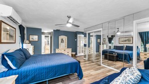 A bedroom with a large bed, a sofa, a mirror, and a ceiling fan.