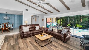 A spacious living room with a large sectional sofa, a wooden coffee table, and a dining area with a blue tablecloth.