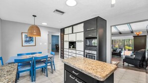 A modern kitchen with granite countertops, black cabinetry, and a dining area with blue chairs and a table.
