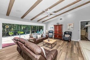 A spacious living area with a large window, a ceiling fan, and a wooden floor.