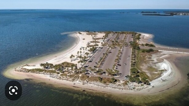 An aerial view of a coastal property with a parking lot, beach, and clear blue sky.