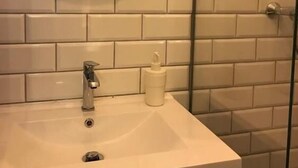 Ett badrum med ett vitt handfat, en rund spegel och en duschkabin med glasväggar.