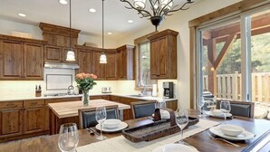 A modern kitchen with wooden cabinets, a central island, and a dining area set for six. - Golf Views, Game Room & Suncadia Pool Access (Cle Elum)