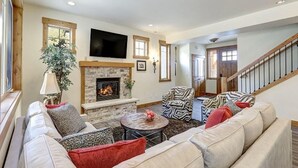 A cozy living room with a fireplace, a sofa set, a patterned armchair, and a television mounted on the wall. - Golf Views, Game Room & Suncadia Pool Access (Cle Elum)