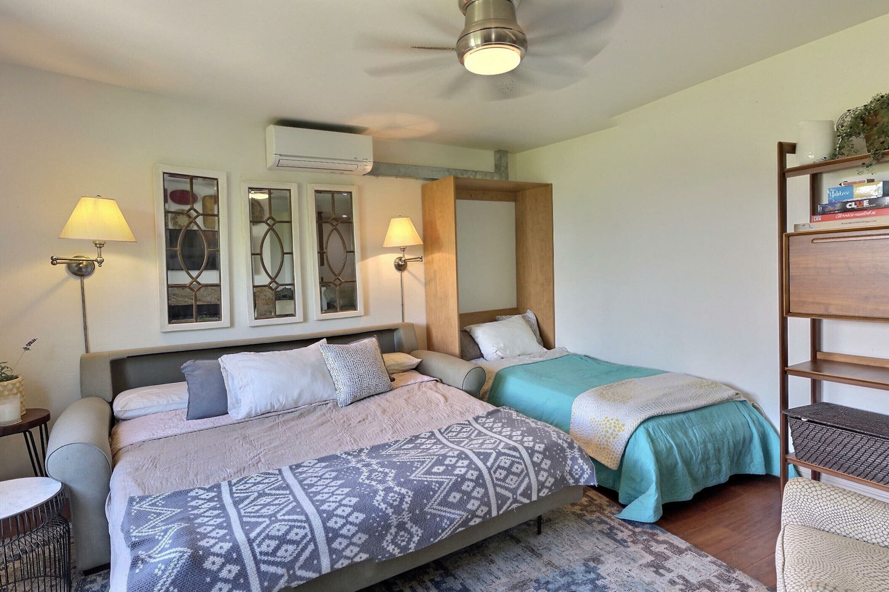 Un dormitorio con dos camas, un ventilador de techo, lámparas de pared y una estantería.