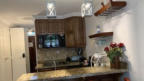 A kitchen with granite countertops, wooden cabinets, a microwave, a toaster, and a sink. There are two pendant lights above the island. - JAMAICA ON THE BEACH (Ocho Rios)