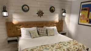 A bedroom with a wooden headboard, a bed with white bedding and patterned pillows, two wall-mounted lanterns, and a nautical-themed wall decoration. - JAMAICA ON THE BEACH (Ocho Rios)