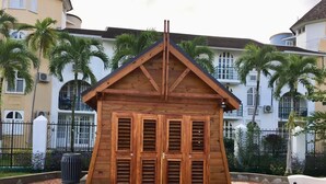 A wooden structure with a triangular roof and multiple shutters, surrounded by a paved area and palm trees. - JAMAICA ON THE BEACH (Ocho Rios)