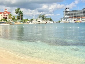 Uma praia com águas cristalinas, um cruzeiro e um edifício com telhado vermelho.