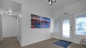 Un pasillo amplio con suelo de madera, felpudo azul, puerta con vidrio esmerilado y una obra de arte colgada en la pared.