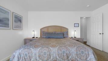 A bedroom with a large bed, two bedside tables, a wooden headboard, and a door.