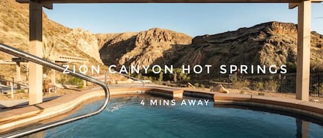 A hot spring pool with wooden pergolas and a mountainous backdrop.