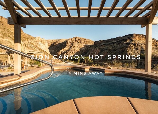 A hot spring pool with wooden pergolas and a mountainous backdrop.