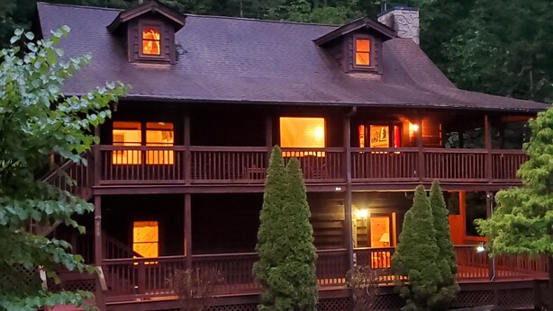 A large, two-story wooden cabin with multiple windows and balconies, surrounded by trees.