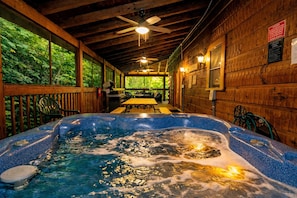 Ein Whirlpool in einer Holz-Blockhütte mit Deckenventilator, Tisch, Stühlen und Blick ins Grüne.