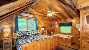 A cozy log cabin bedroom with a bed, a vanity, a ceiling fan, and a sign reading 'Always Kiss Me Goodnight.'