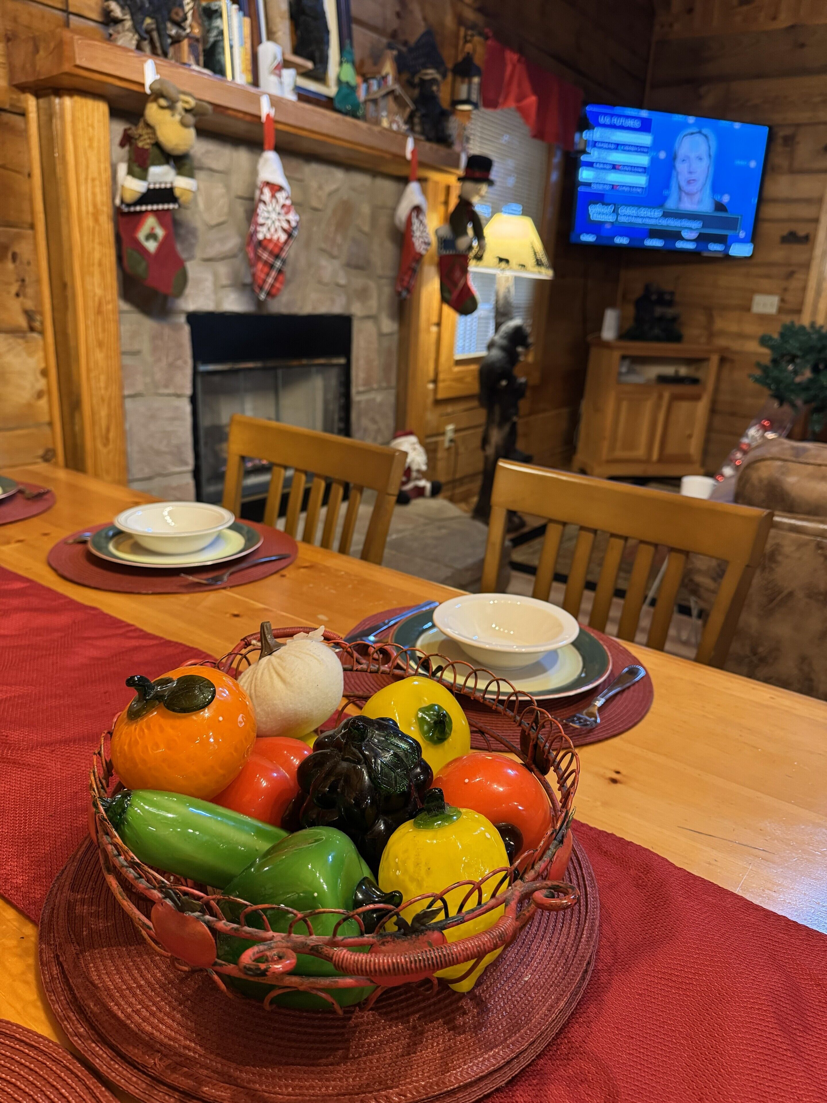 A dining table with a fruit basket, a fireplace, and a television in the background.