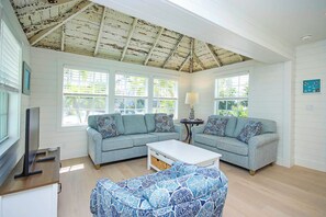 Ein geräumiges Wohnzimmer mit zwei grauen Sofas, einem weißen Couchtisch und einem gemusterten Pouf.