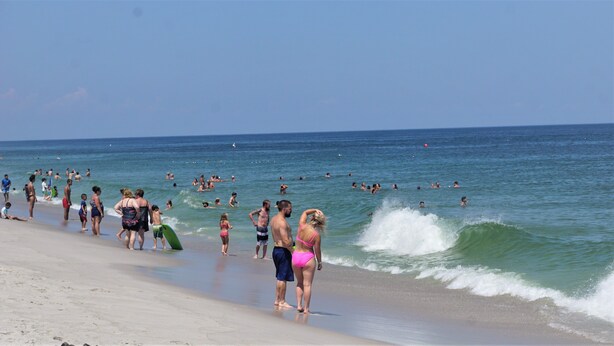 Una playa concurrida, gente nadando y caminando por la orilla.