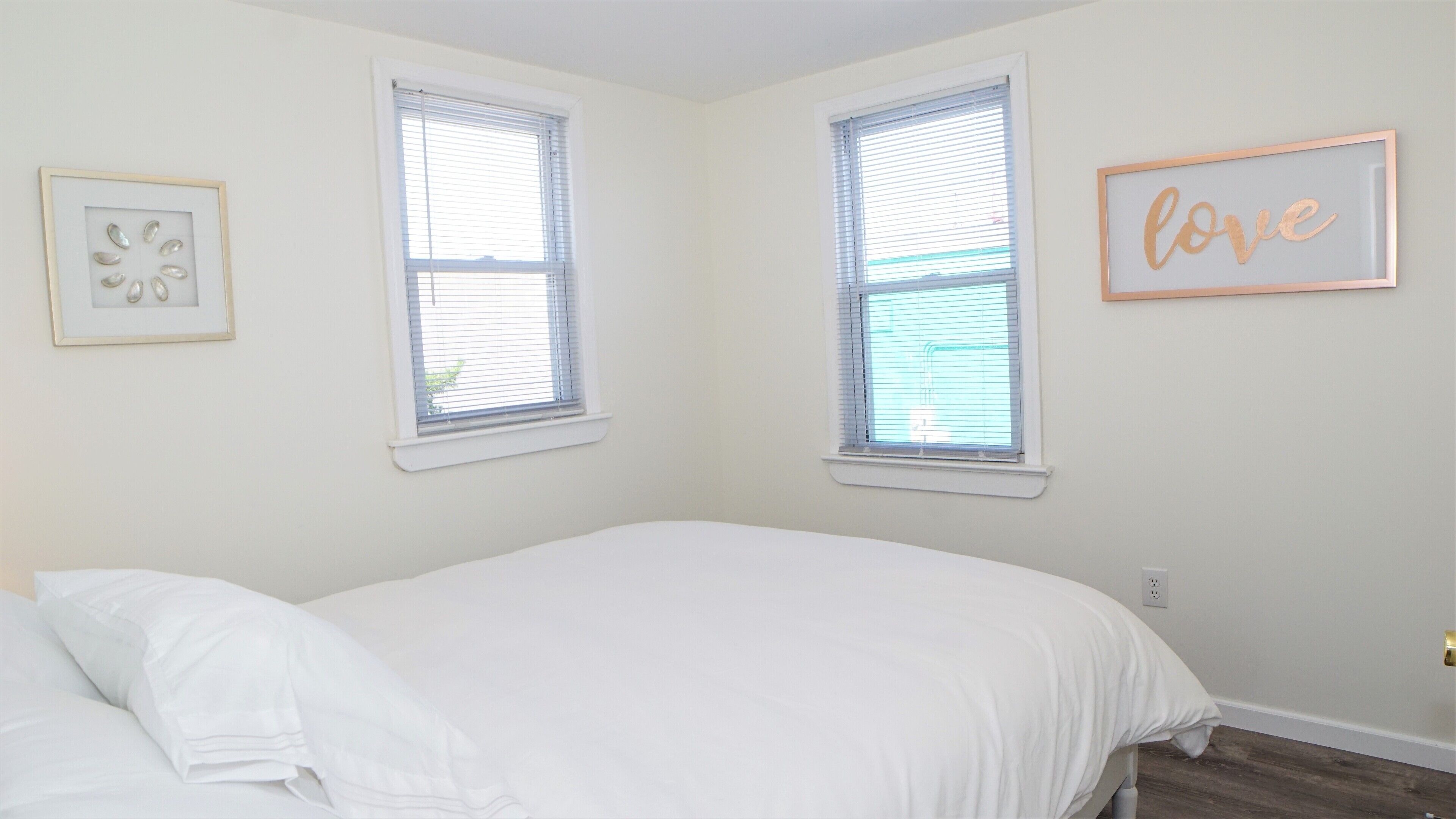 A bedroom with a bed, two windows, and a wall decoration.