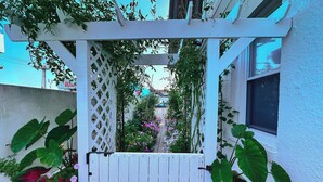 Un portón blanco de madera con diseño de celosía, rodeado de plantas verdes exuberantes y flores vibrantes.