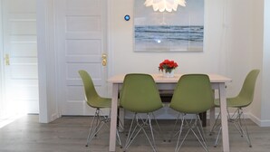 Un comedor con una mesa, cuatro sillas verdes, un jarrón con flores rojas y una obra de arte en la pared que representa el océano.