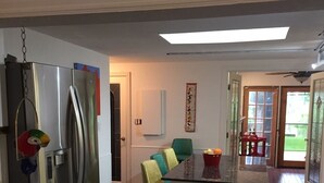 Una cocina moderna con un refrigerador de acero inoxidable, una isla central con taburetes de bar y un comedor con una silla verde.