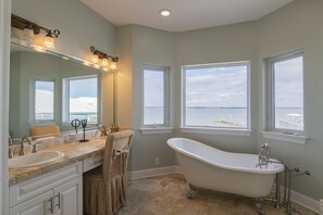 A bathroom with a freestanding bathtub, a large mirror with lights, and a view of the water. - ocean sounds retreat (Navarre)