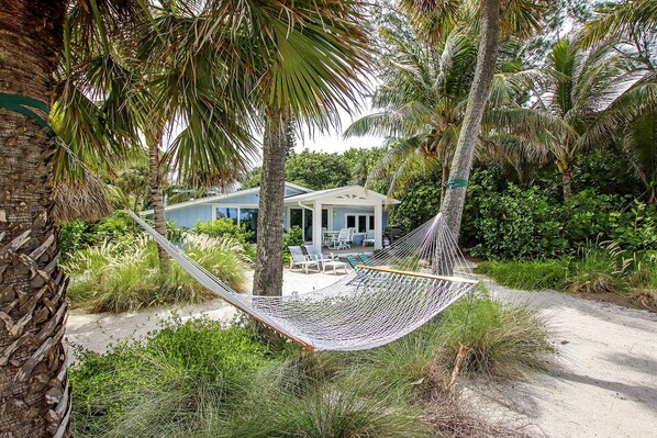 A hammock between palm trees overlooking a house with a pool and outdoor seating.