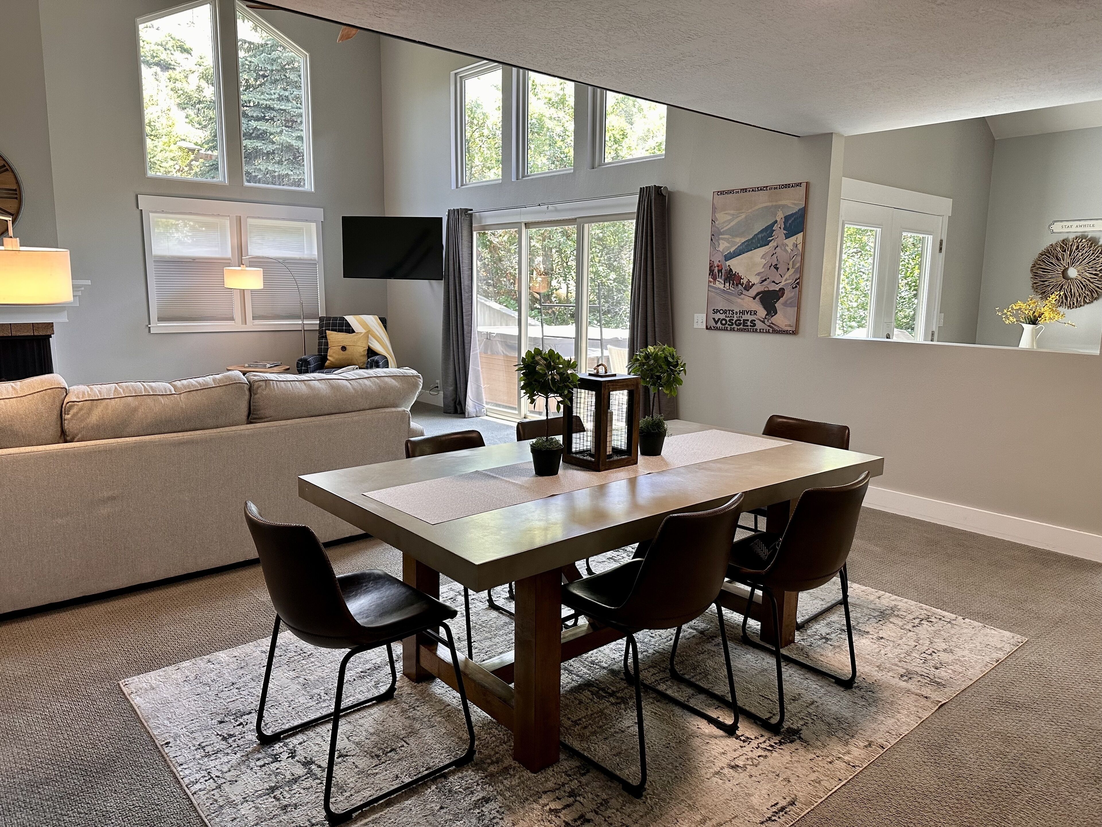 A modern living room with a dining area, large windows, and a flat-screen TV.