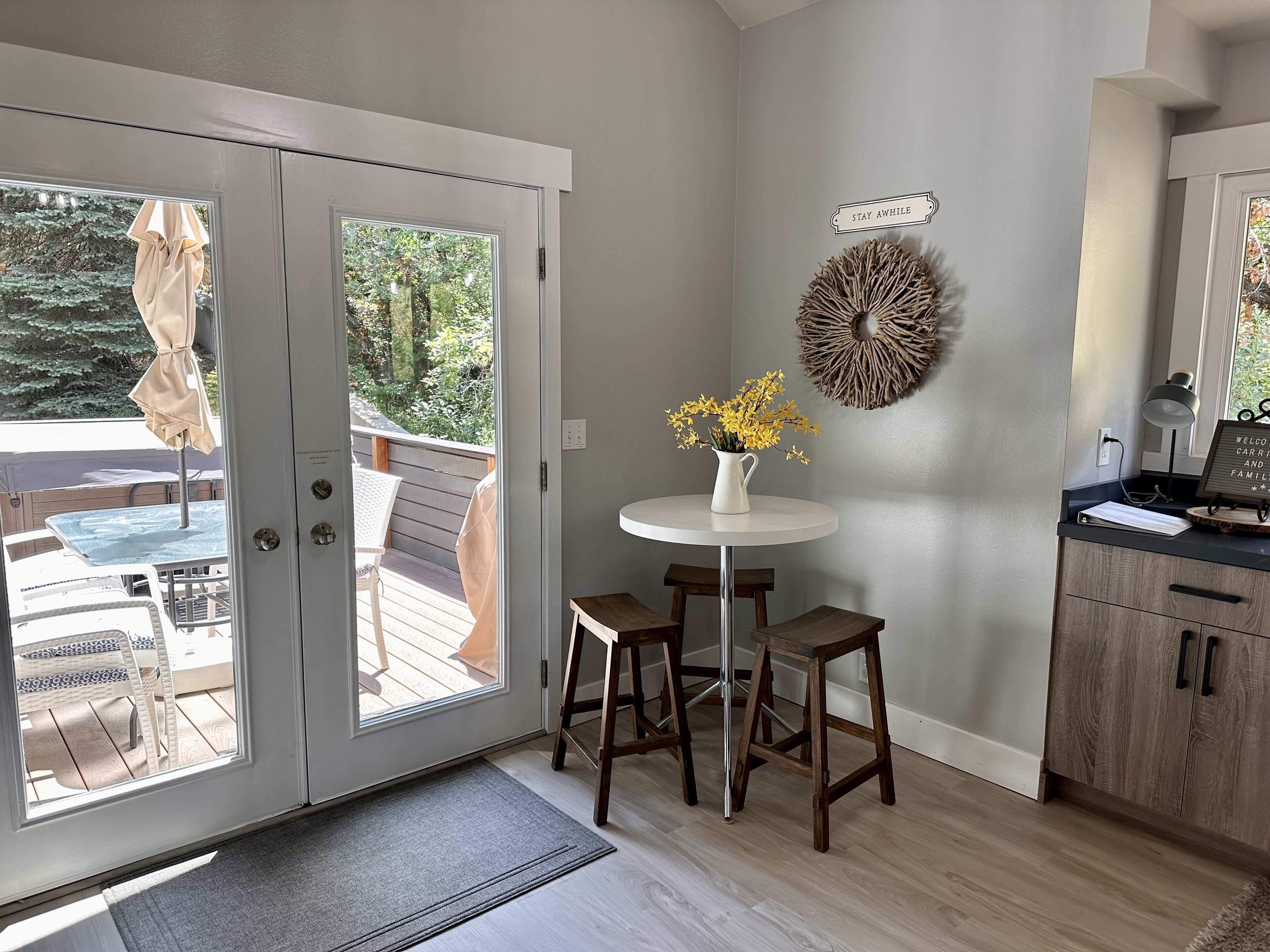 A room with a sliding glass door leading to an outdoor deck, a small round table with a vase of flowers, and a wall-mounted decorative piece.