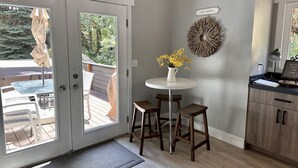 A room with a sliding glass door leading to an outdoor deck, a small round table with a vase of flowers, and a wall-mounted decorative piece.