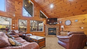 A cozy living room with leather sofas, a stone fireplace, and large windows. - Bottoms Up double deck dock w/ slide, hot tub, near famous 'jumping bridge' (LaFollette)