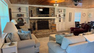 A living room with a fireplace, sofas, a TV, and a dining area with chairs.