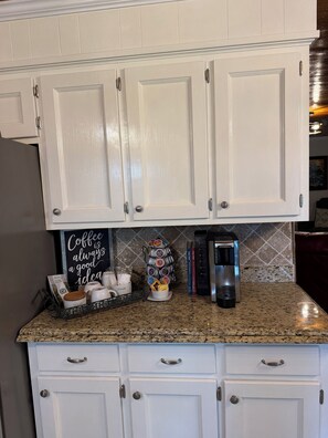 A kitchen with white cabinets, a coffee maker, a mug rack, and a coffee sign.