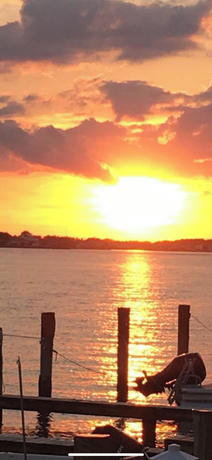 A sunset over a body of water with a wooden dock and a boat.