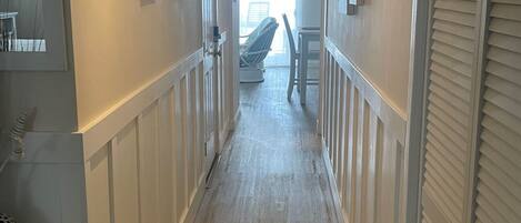 A hallway with wooden floors, white wainscoting, and framed artwork on the walls.