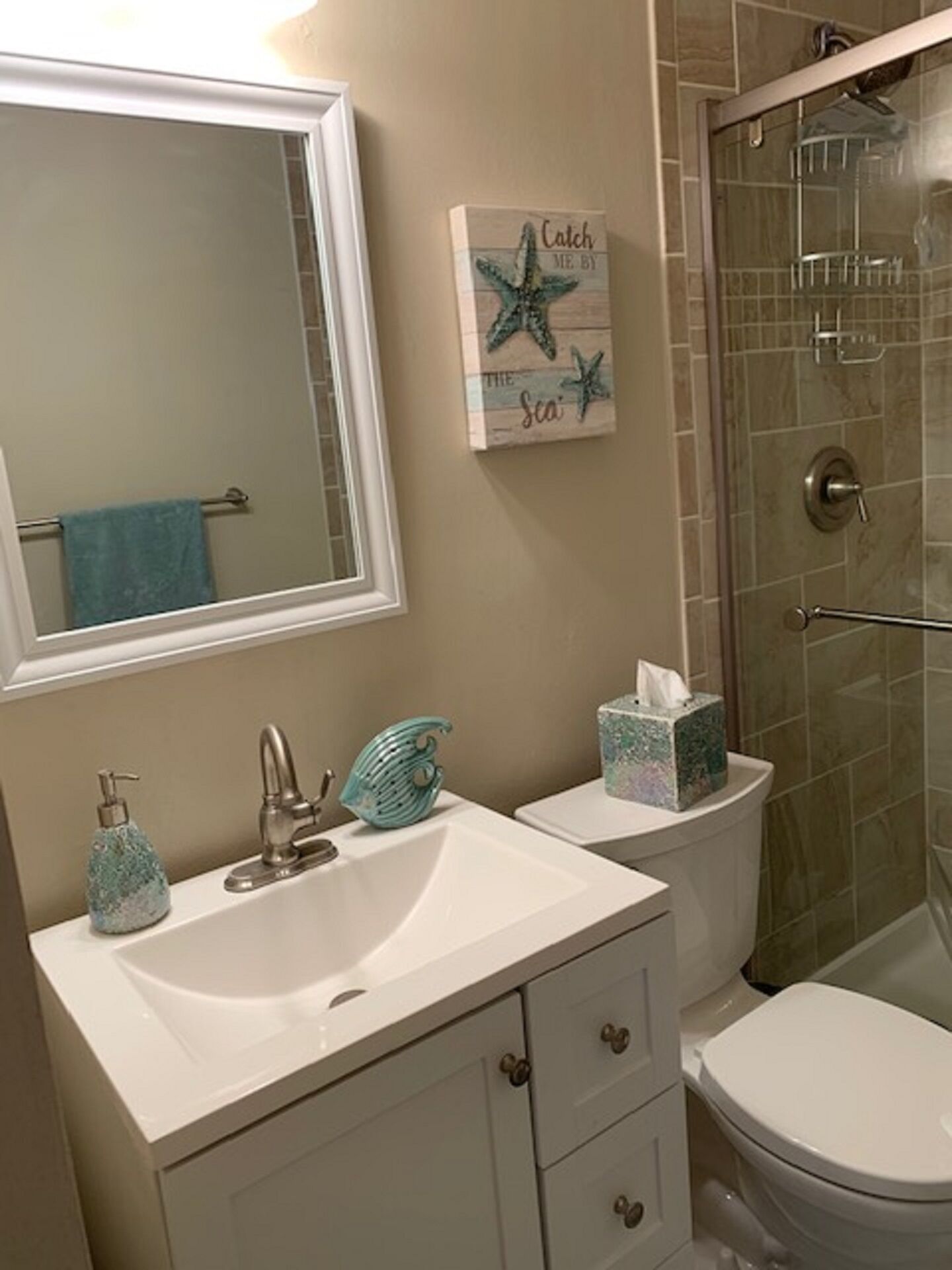 Une salle de bain avec un lavabo blanc, un miroir, un porte-serviettes, une cabine de douche et des toilettes.