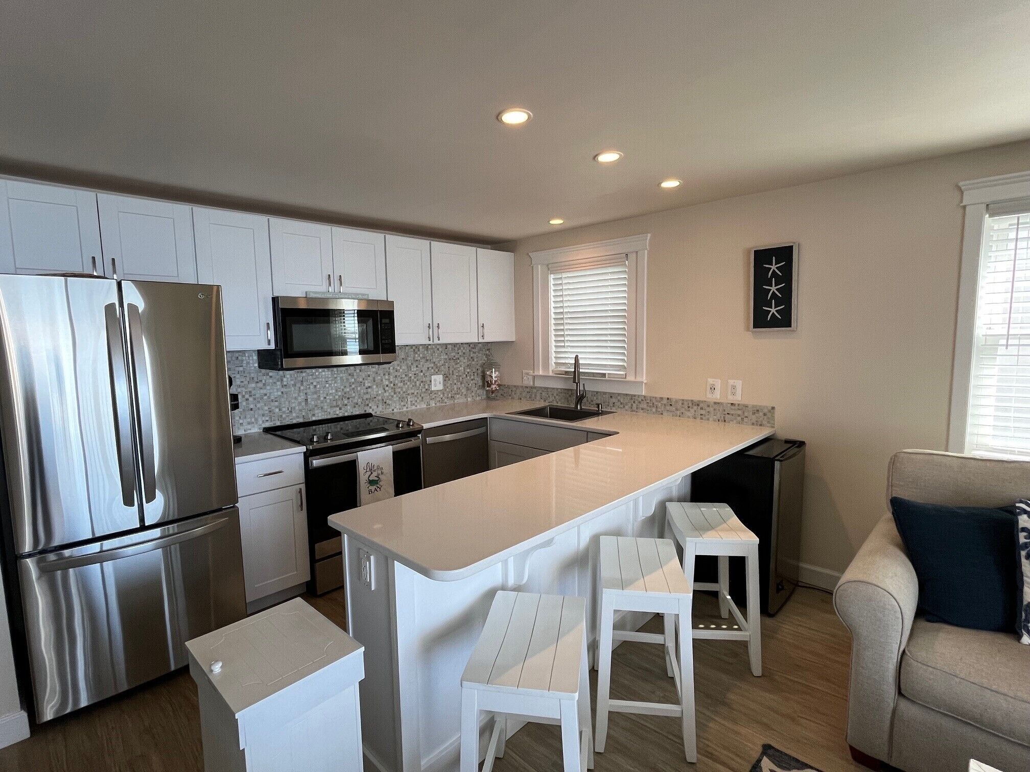 A modern kitchen with stainless steel appliances, white cabinetry, and a central island with bar stools.