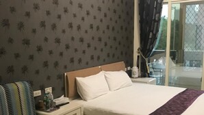Une chambre d’hôtel avec un lit, un fauteuil à rayures, une table de chevet et une fenêtre avec des rideaux.
