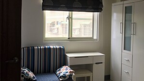 Une chambre à coucher comprenant un lit, un bureau, une armoire et une fenêtre donnant sur les bâtiments environnants.
