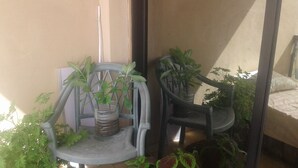 Un balcon avec deux chaises, dont une ornée d’un pot de fleurs et l’autre d’une plante suspendue.