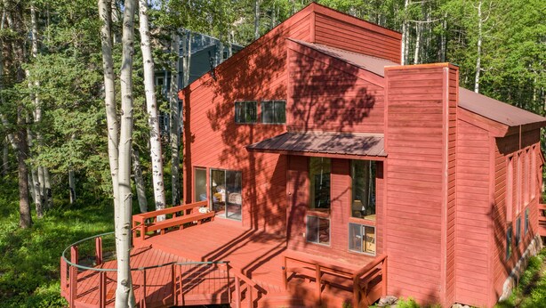 Une cabane en bois rouge avec une terrasse, entourée d’arbres.