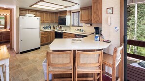Une cuisine compacte avec des meubles en bois, un réfrigérateur blanc et un coin repas comprenant deux chaises en osier.