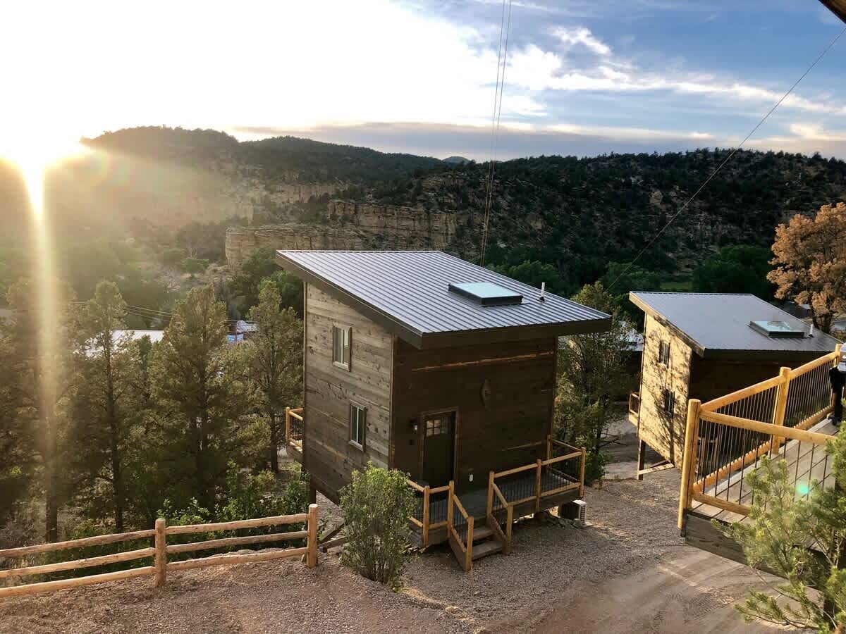 A rustic cabin with a metal roof, surrounded by a wooden fence, set against a mountainous backdrop.