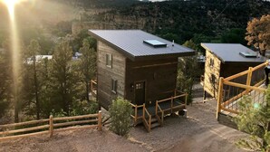 A rustic cabin with a metal roof, surrounded by a wooden fence, set against a mountainous backdrop.