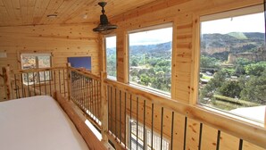 Una stanza in una baita di legno con un letto, ampie finestre e una ringhiera da balcone.